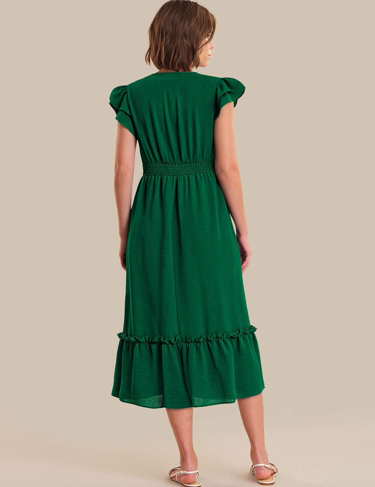 Woman wearing a green dress with ruffled sleeves and bottom hem on a beige background