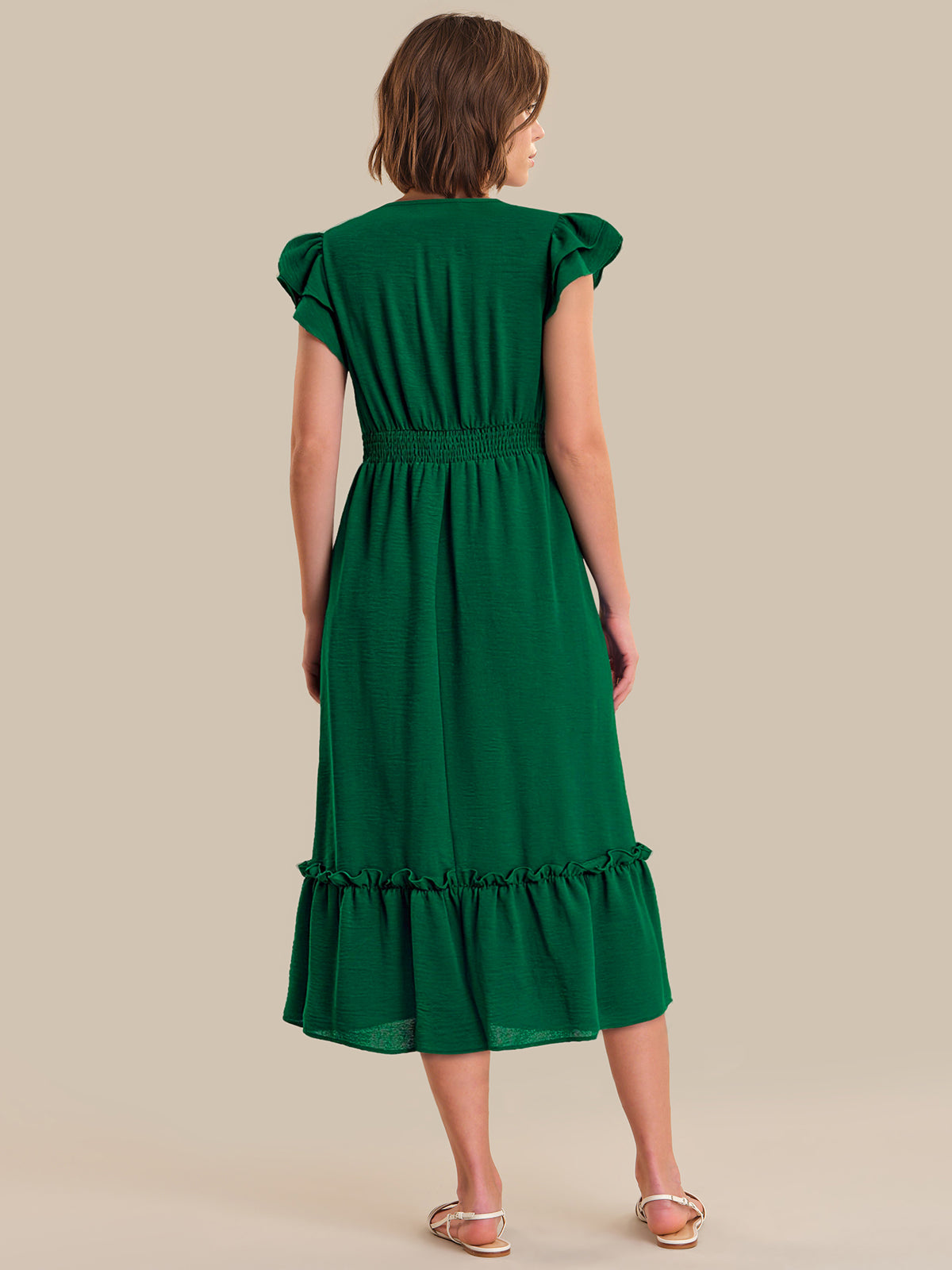 Woman wearing a green dress with ruffled sleeves and bottom hem on a beige background