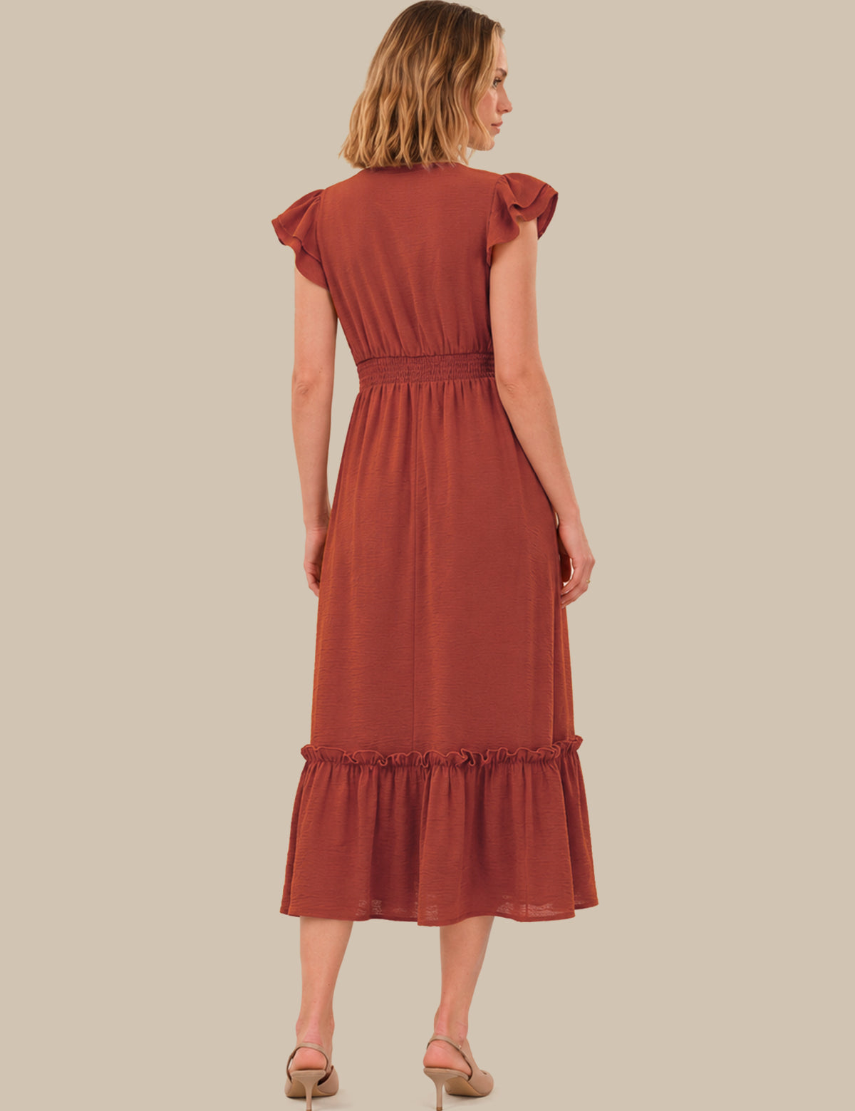 A woman shown from the back wearing a rust-colored midi dress with ruffled cap sleeves, a gathered waist, and a ruffled hem, paired with beige heels against a solid beige background.
