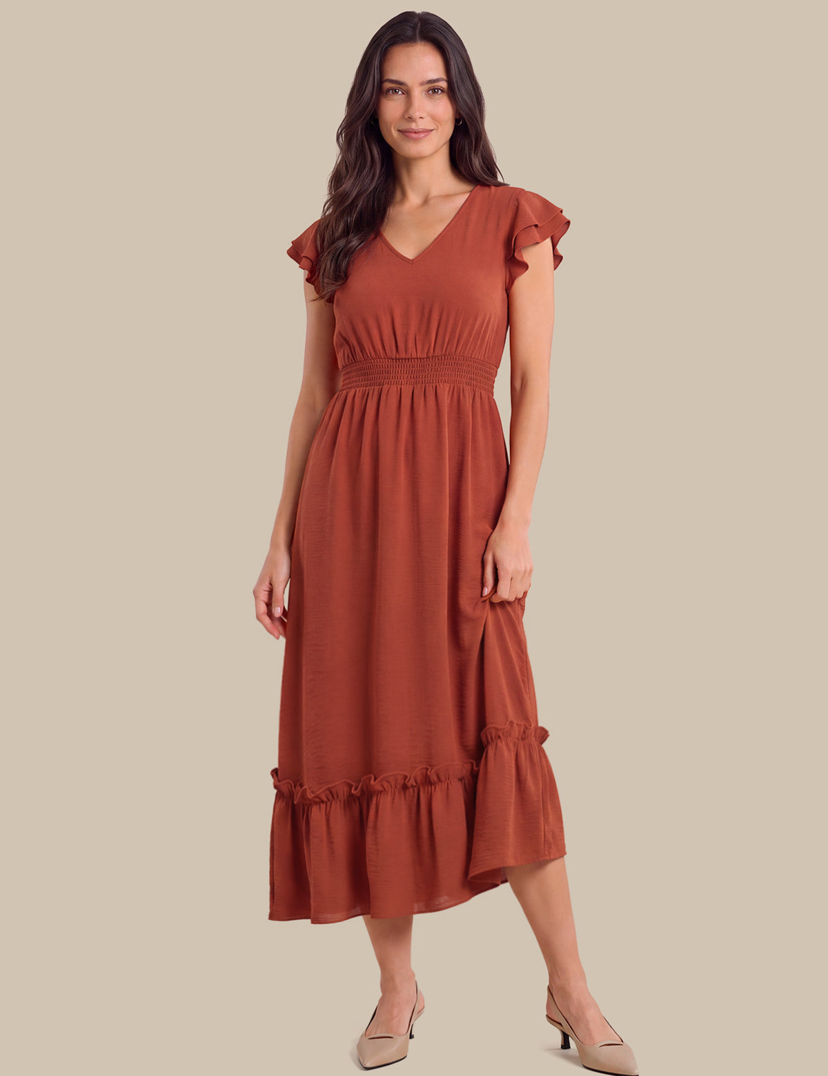A woman modeling a rust-colored midi dress with ruffled cap sleeves, a V-neckline, a gathered waist, and a tiered hem, paired with beige heels against a solid beige background.