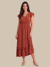 A woman modeling a rust-colored midi dress with ruffled cap sleeves, a V-neckline, a gathered waist, and a tiered hem, paired with beige heels against a solid beige background.