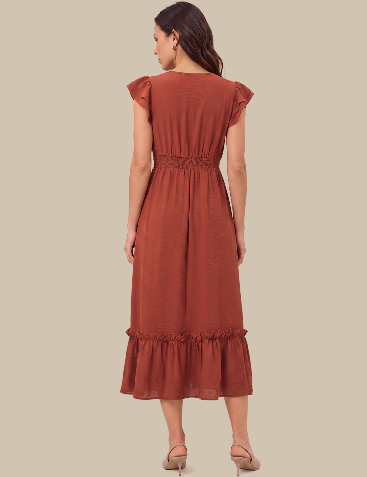 A woman shown from the back wearing a rust-colored midi dress with ruffled cap sleeves, a smocked waist, and a ruffled hem, paired with beige high-heeled sandals against a solid beige background.