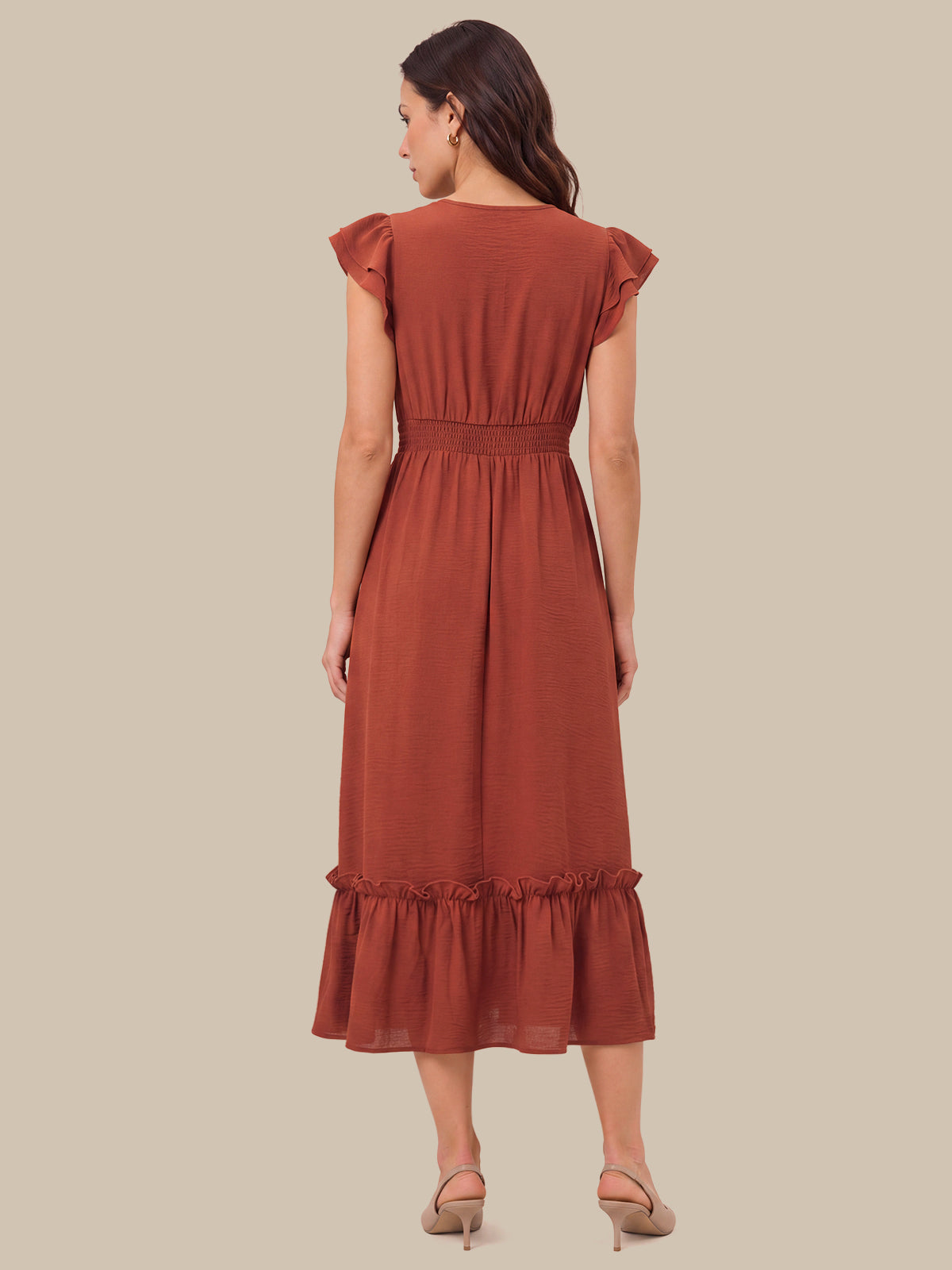 A woman shown from the back wearing a rust-colored midi dress with ruffled cap sleeves, a smocked waist, and a ruffled hem, paired with beige high-heeled sandals against a solid beige background.