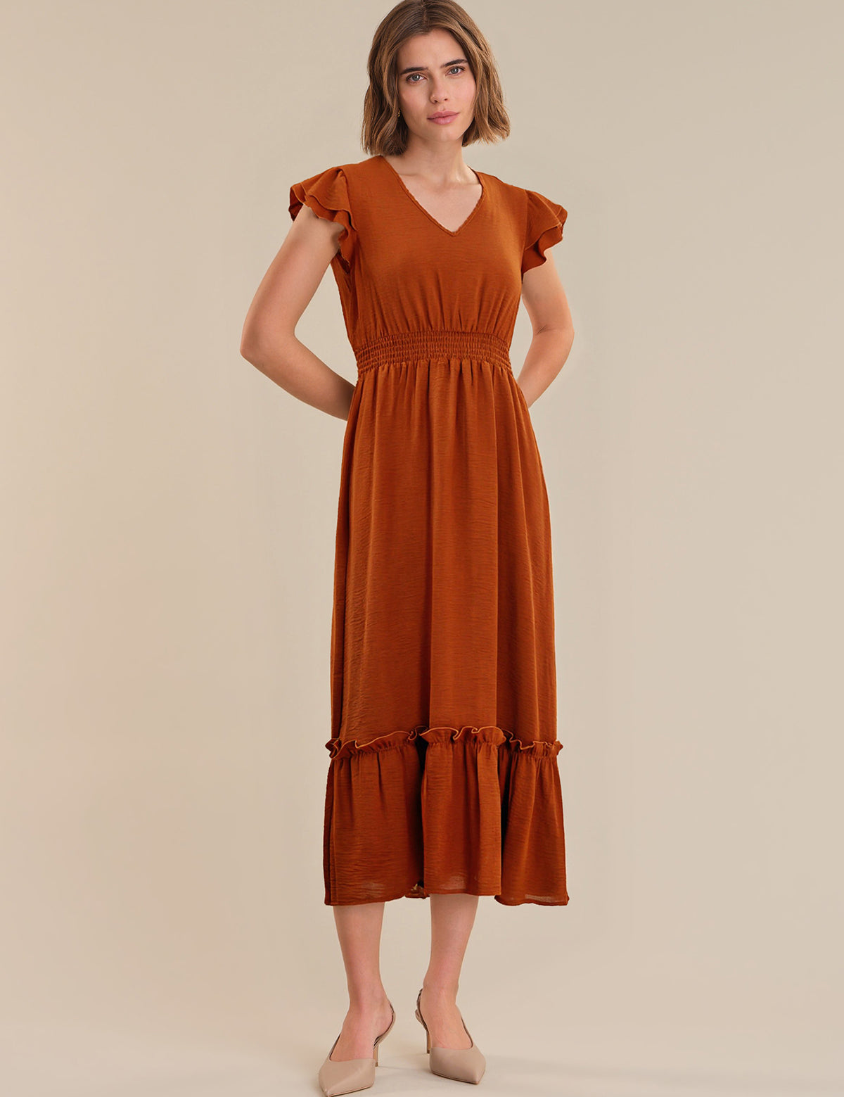 Woman wearing a rust-colored dress with ruffled sleeves on a beige background