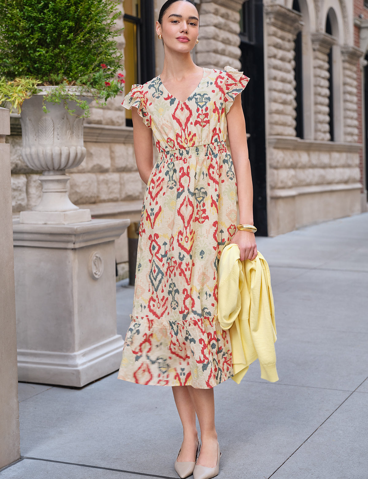 Woman in a floral dress holding a yellow jacket on a city street.