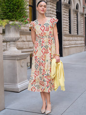 Woman in a floral dress holding a yellow jacket on a city street.