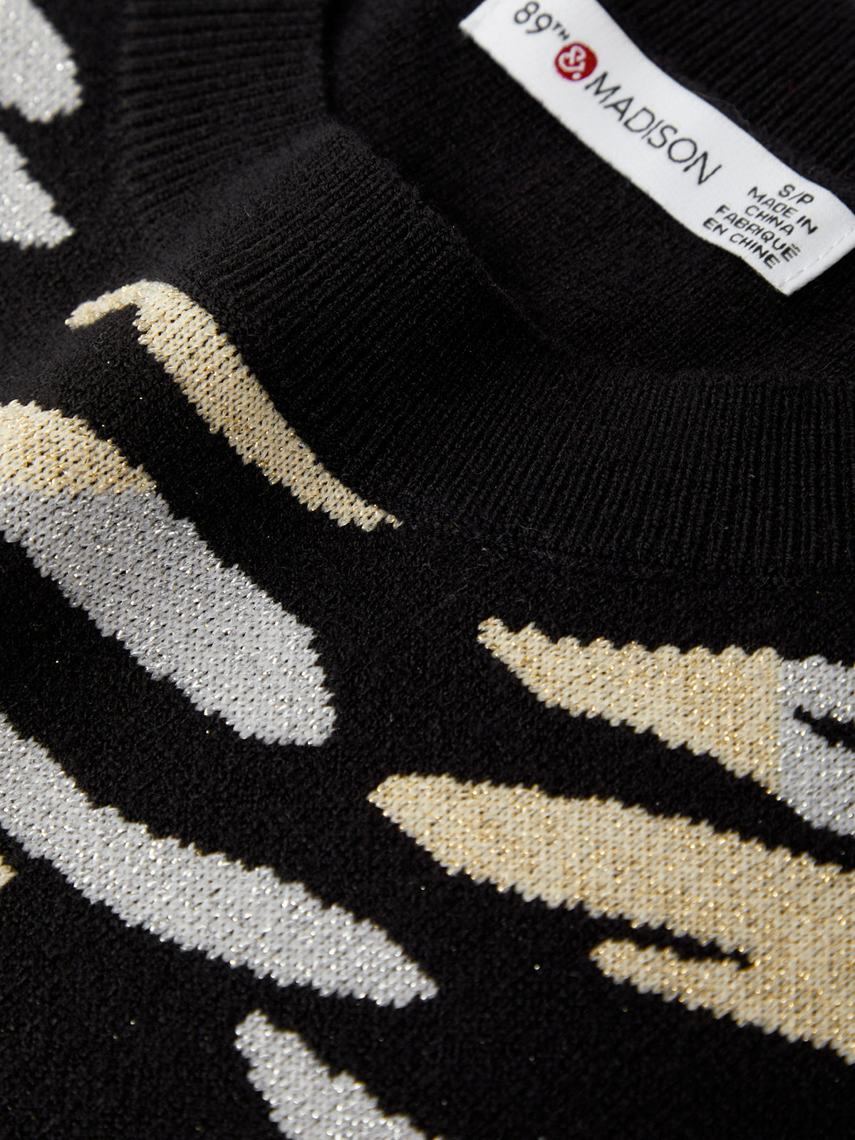 Close-up of a black sweater with beige and white pattern, featuring a brand label.