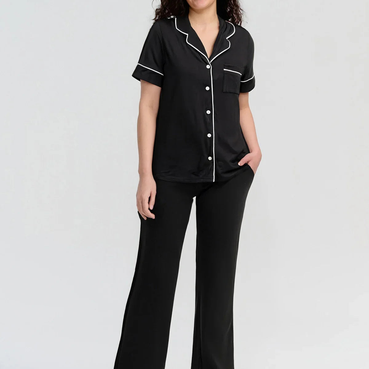Woman wearing a black pajama set with white piping on a white background