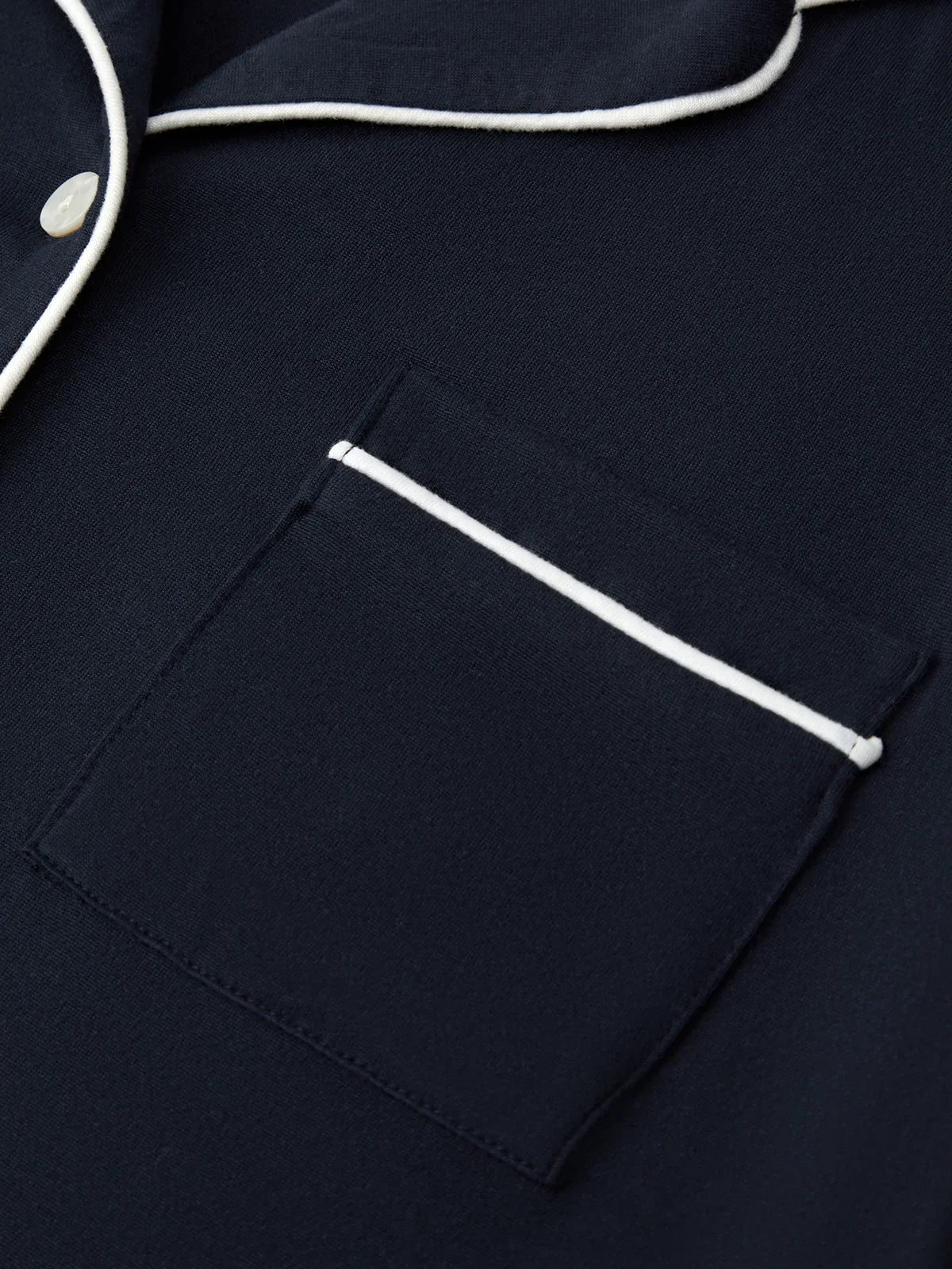 Navy blue pajama top with white piping on a matching fabric background