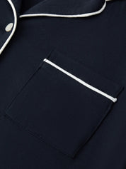 Navy blue pajama top with white piping on a matching fabric background