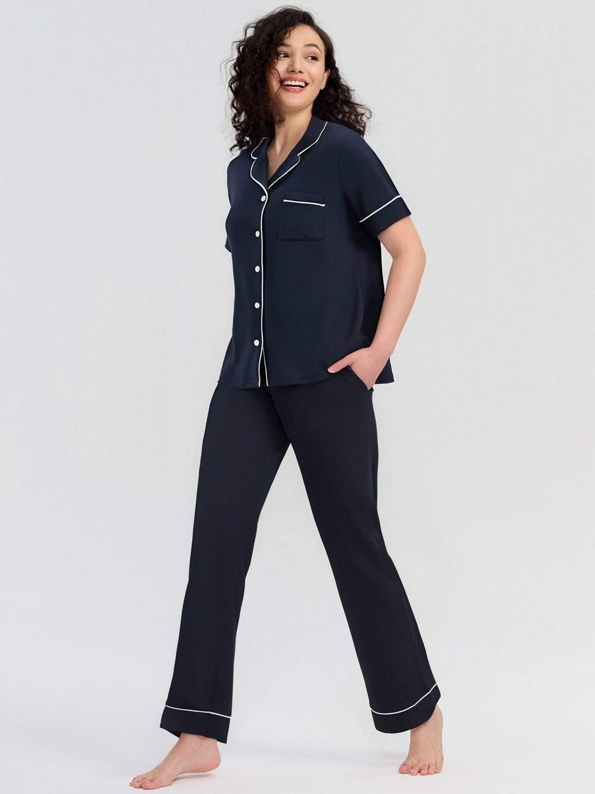 Woman wearing navy pajamas with white piping on a white background