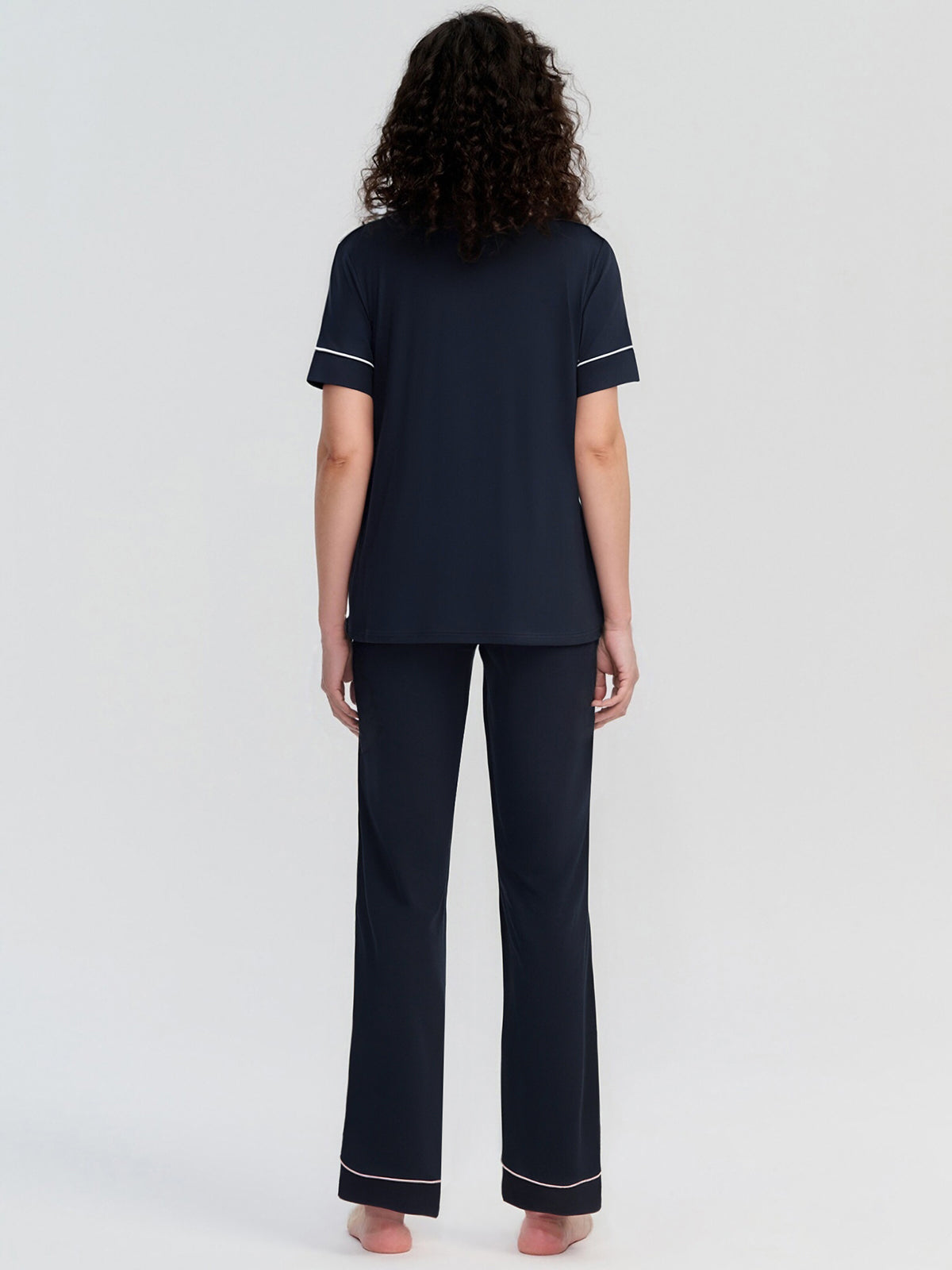 Person wearing a navy pajama set with white piping on a light gray background