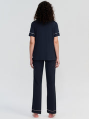 Person wearing a navy pajama set with white piping on a light gray background