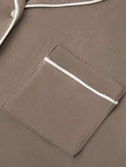 Close-up of a taupe brown garment featuring a chest pocket with white piping and a matching white button, showing the fabric texture.