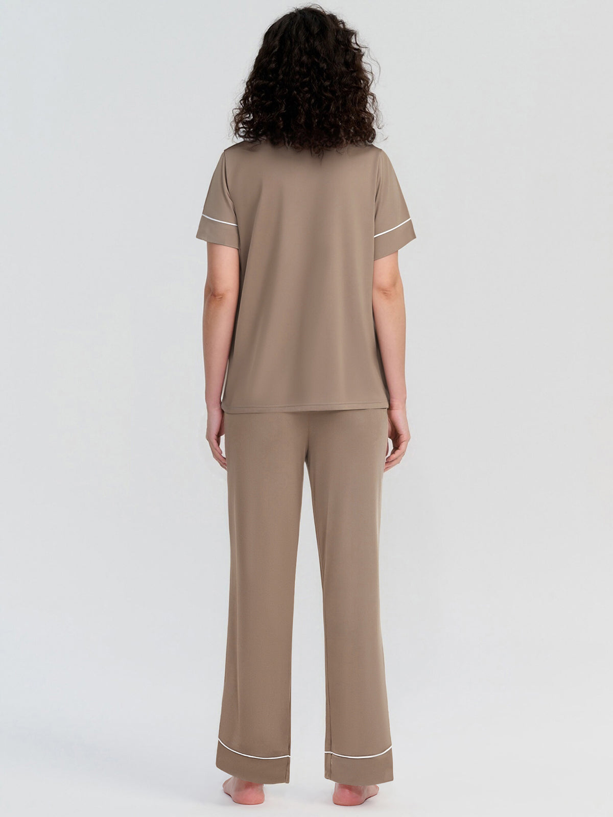 Woman wearing a beige pajama set with white piping on a light gray background