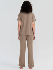 Woman wearing a beige pajama set with white piping on a light gray background