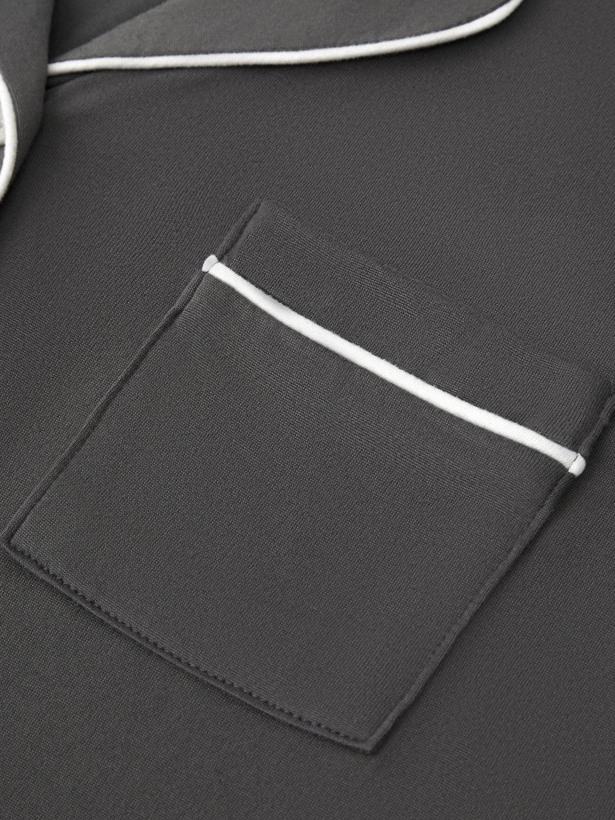 Close-up of a dark gray fabric garment featuring a pocket with a contrasting white piping trim.