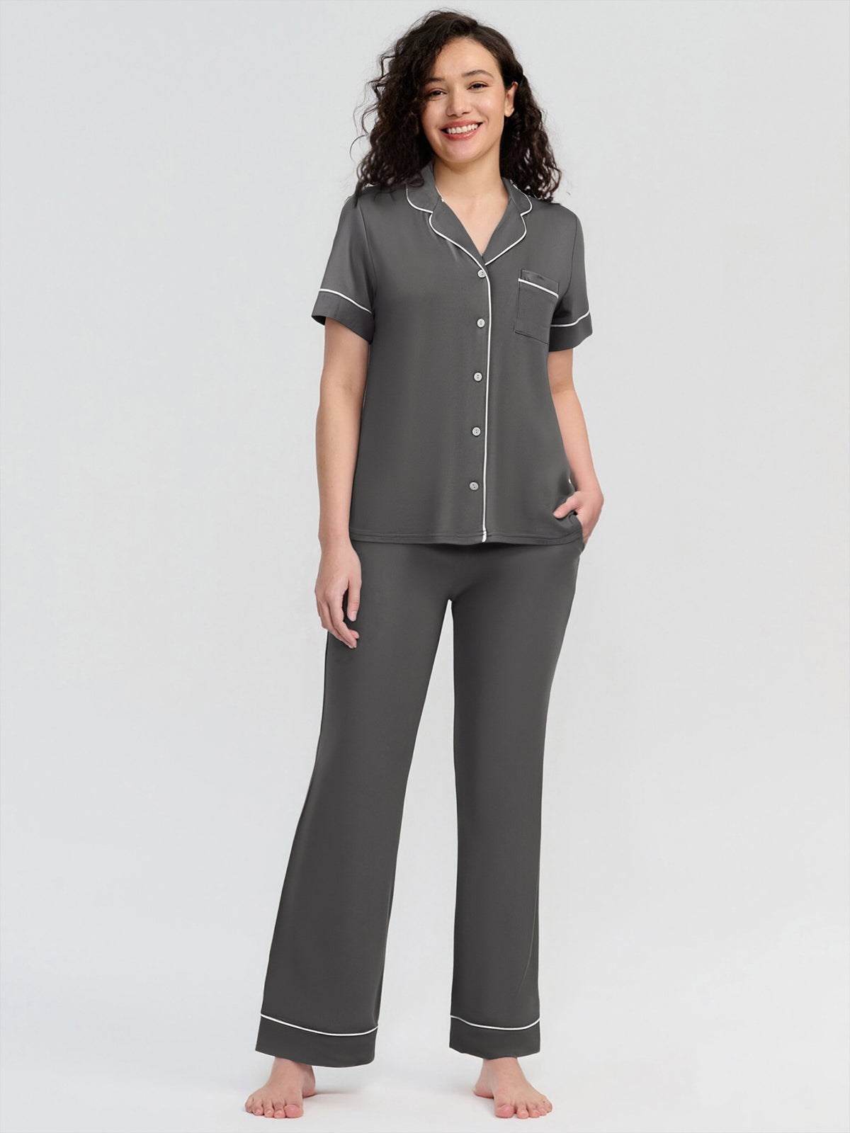 Woman wearing a gray pajama set with white piping on a white background