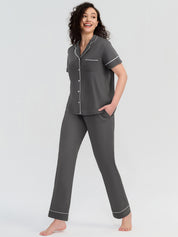 Woman wearing a gray pajama set with white piping on a white background