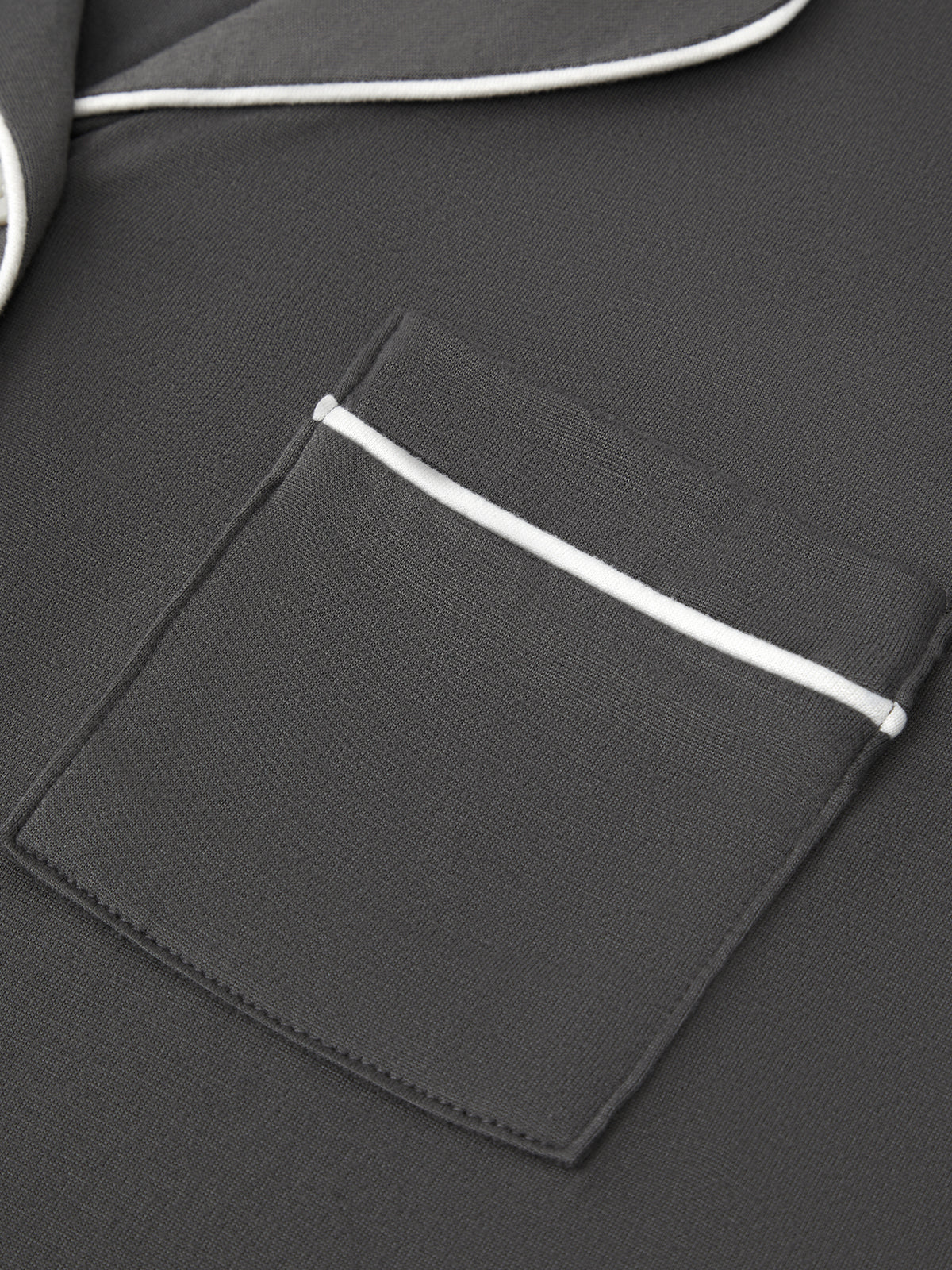 Close-up of a dark gray jacket with a pocket and white piping detail.