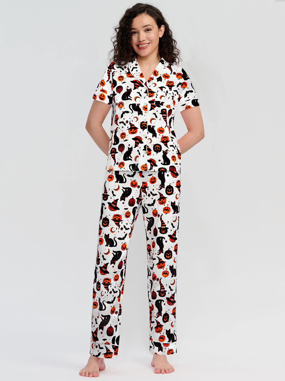 Woman wearing a pajama set with cat and pumpkin pattern on a white background