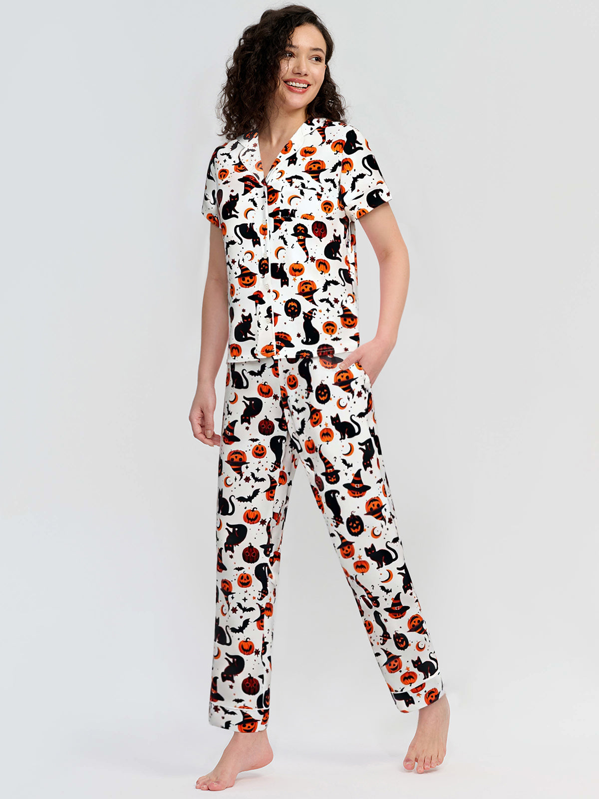 Woman wearing a pajama set with a cat and pumpkin pattern on a white background