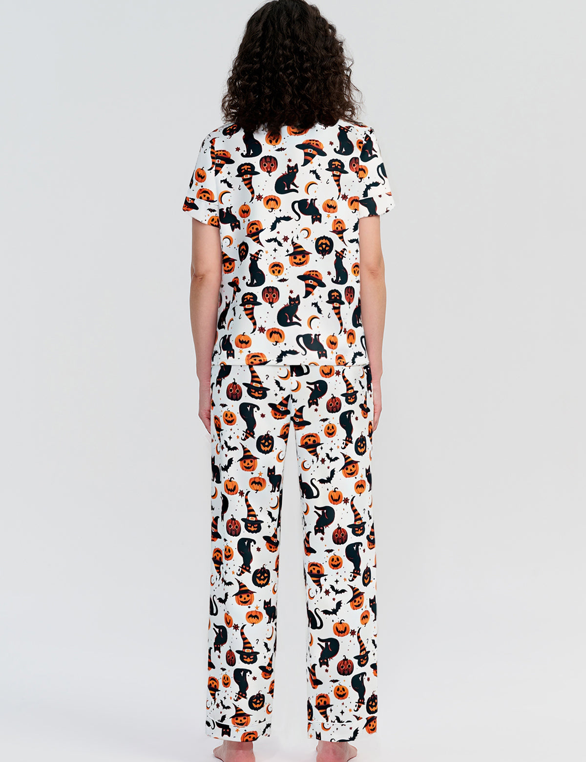 Person wearing a pajama set with a cat and pumpkin pattern on a white background