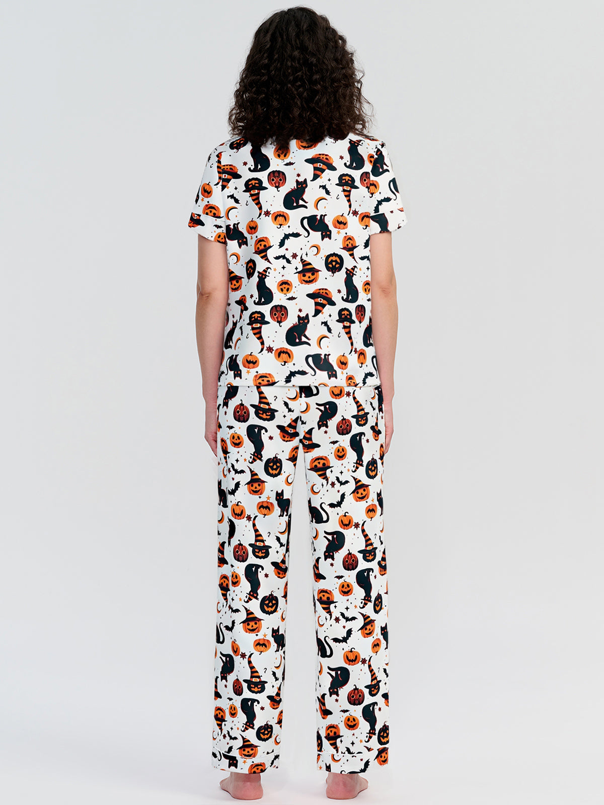 Person wearing a pajama set with a cat and pumpkin pattern on a white background
