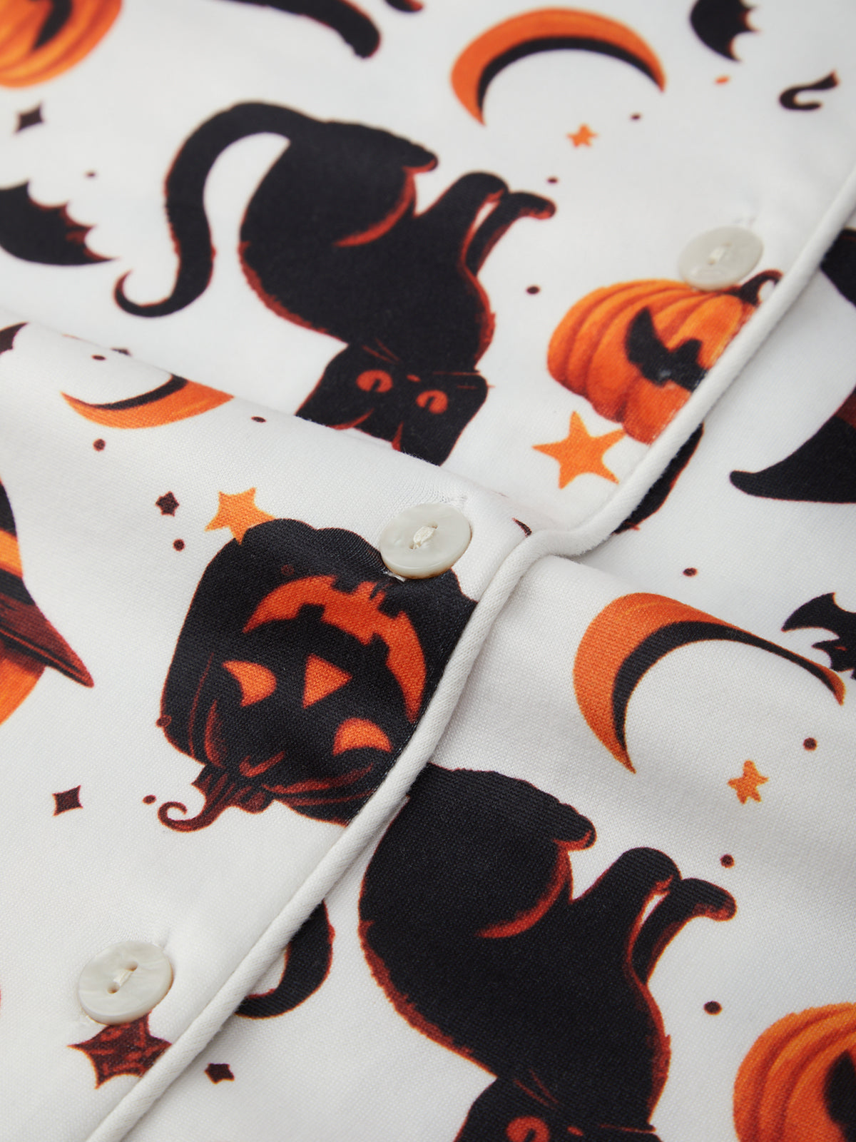 Close-up of a fabric with Halloween-themed pattern including pumpkins, ghosts, and cats on a white background.