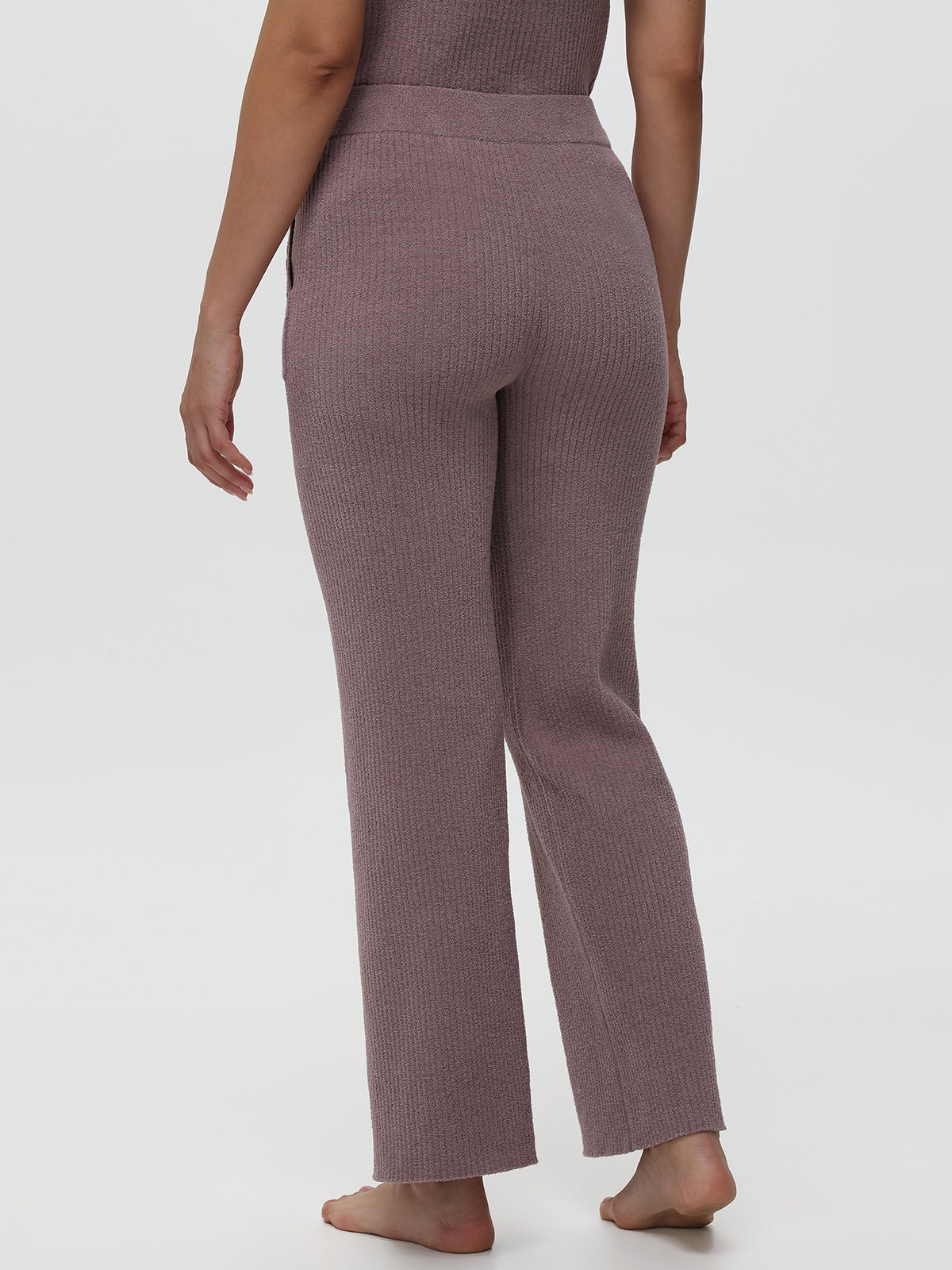 Person wearing ribbed mauve pants on a white background
