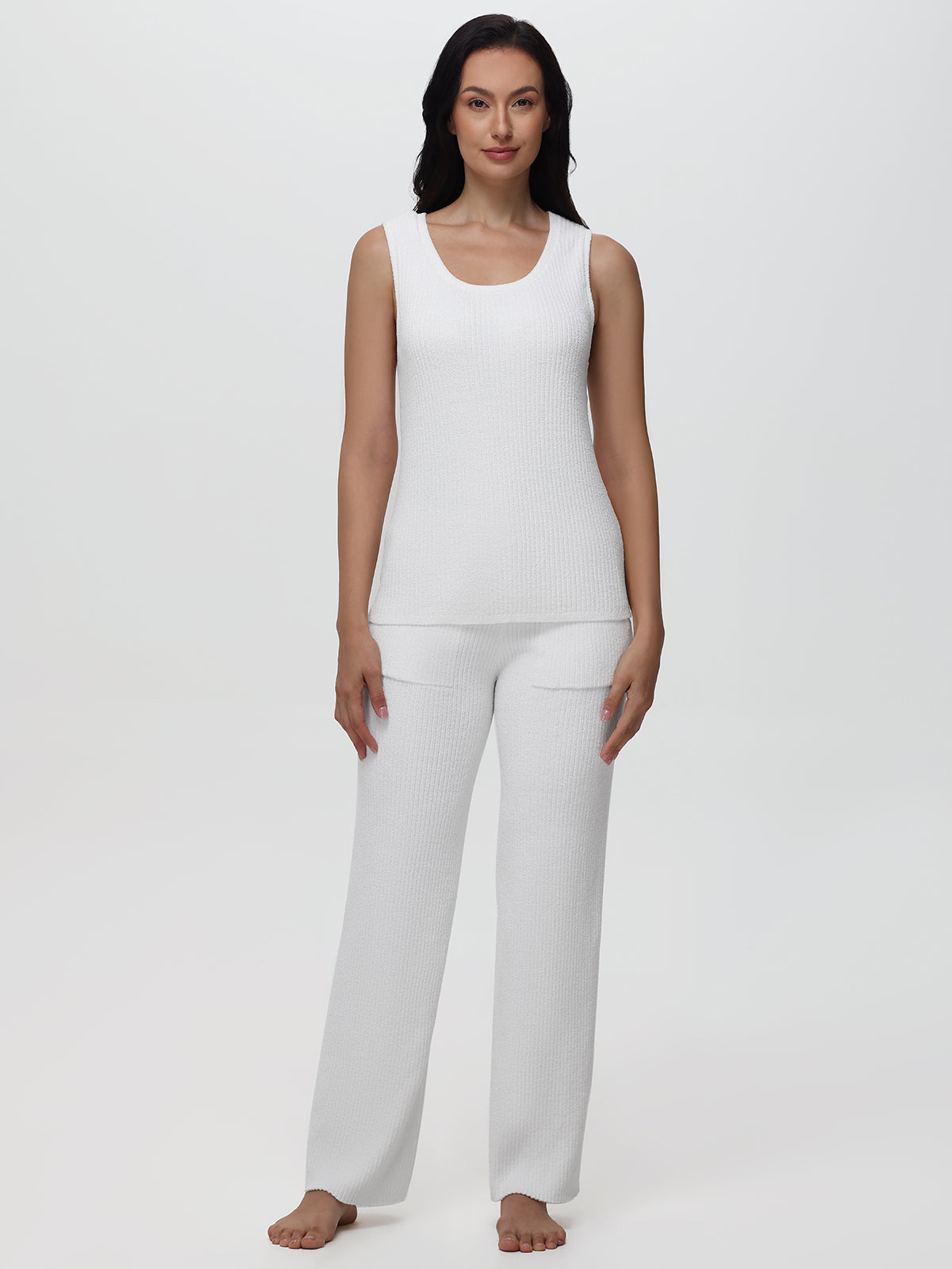 Woman wearing a white sleeveless top and pants on a plain background