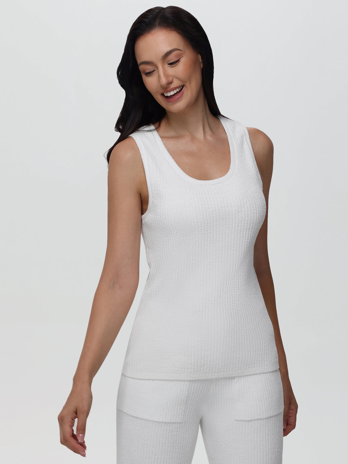 Woman wearing a white sleeveless top and pants on a plain background