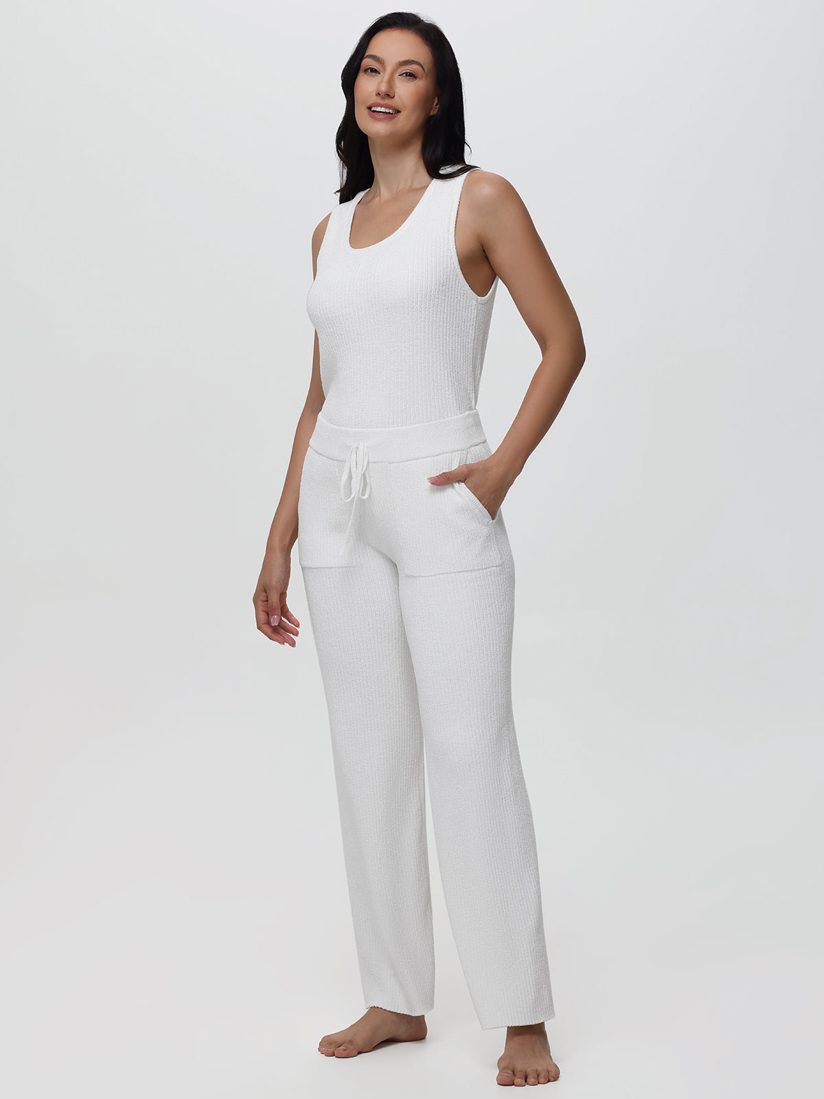 Woman wearing a white sleeveless top and pants on a light gray background