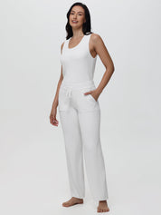 Woman wearing a white sleeveless top and pants on a light gray background