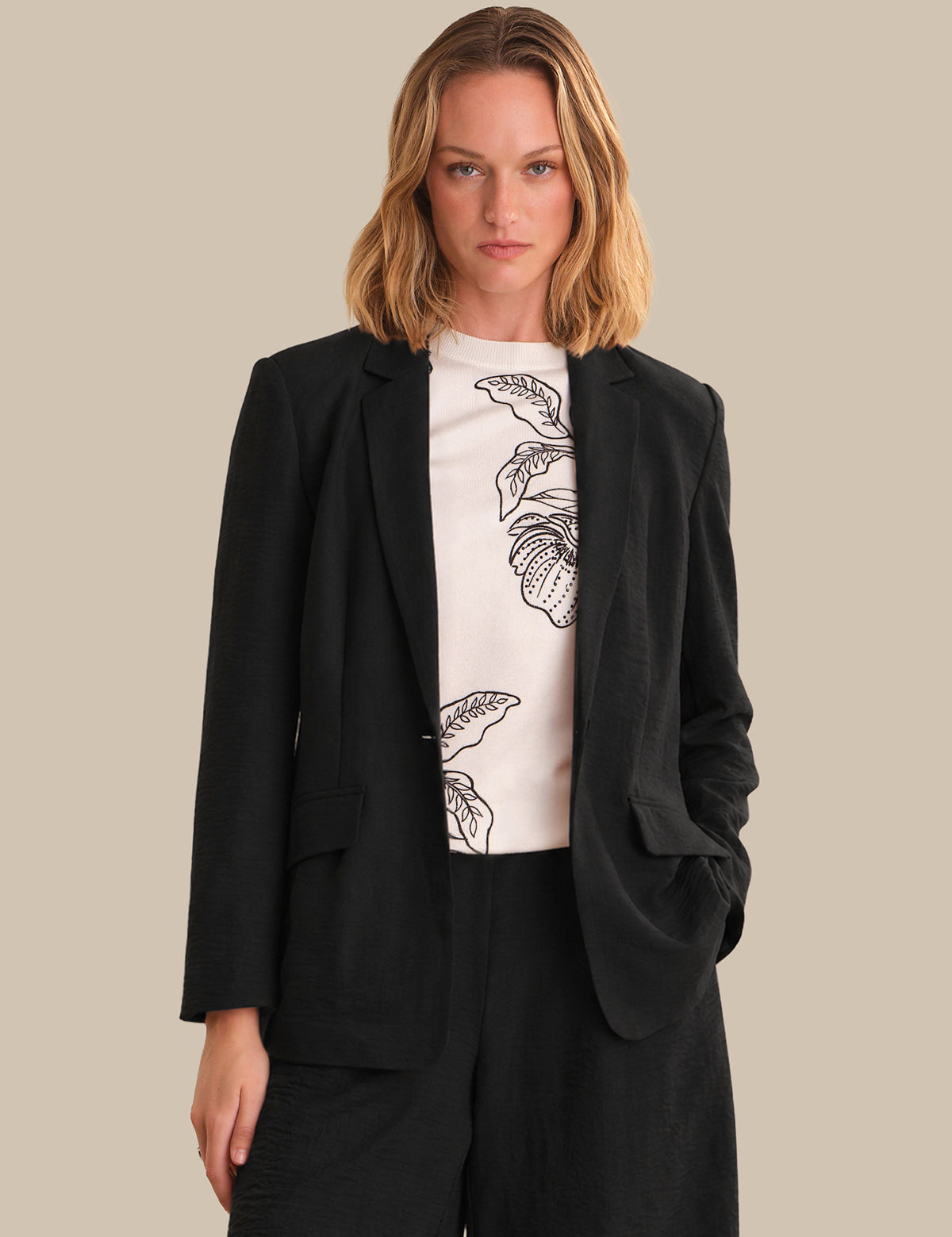 Woman wearing a black blazer over a white t-shirt with a floral design on a beige background