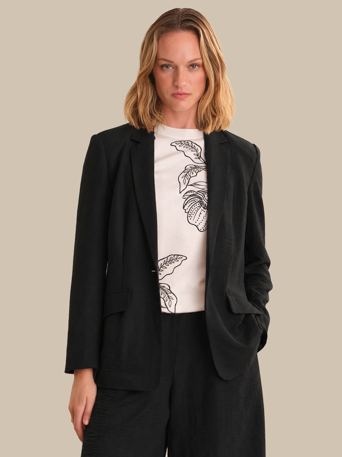 Woman wearing a black blazer over a white t-shirt with a floral design on a beige background