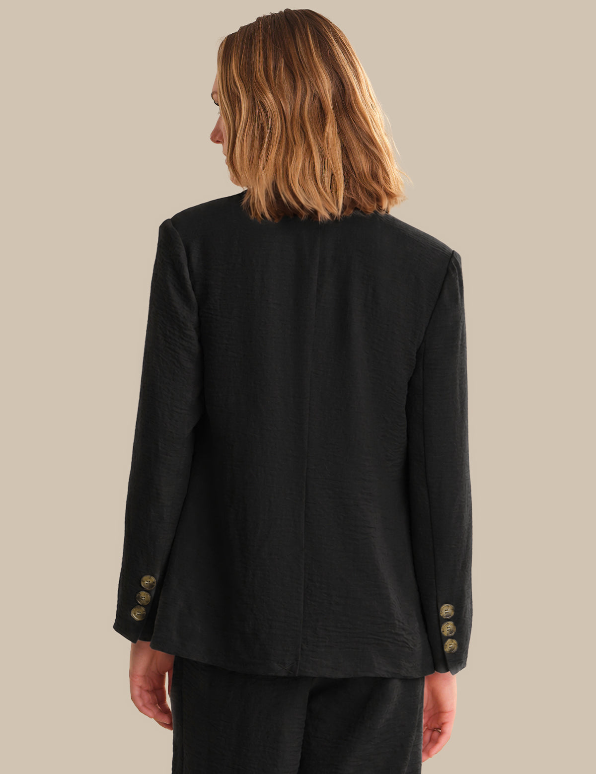 Person wearing a black blazer with gold buttons on a beige background