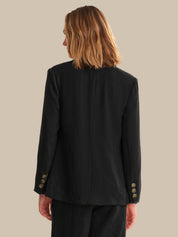 Person wearing a black blazer with gold buttons on a beige background