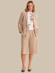 Woman wearing a beige suit with a white shirt featuring black floral patterns on a plain background