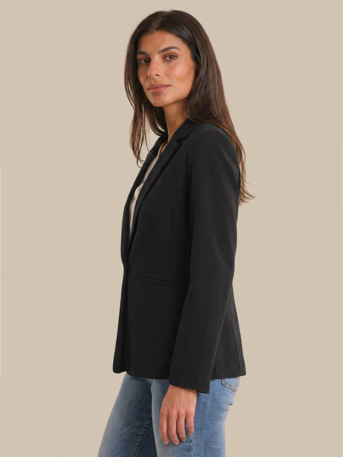 Woman wearing a black blazer and blue jeans on a beige background