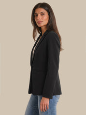 Woman wearing a black blazer and blue jeans on a beige background