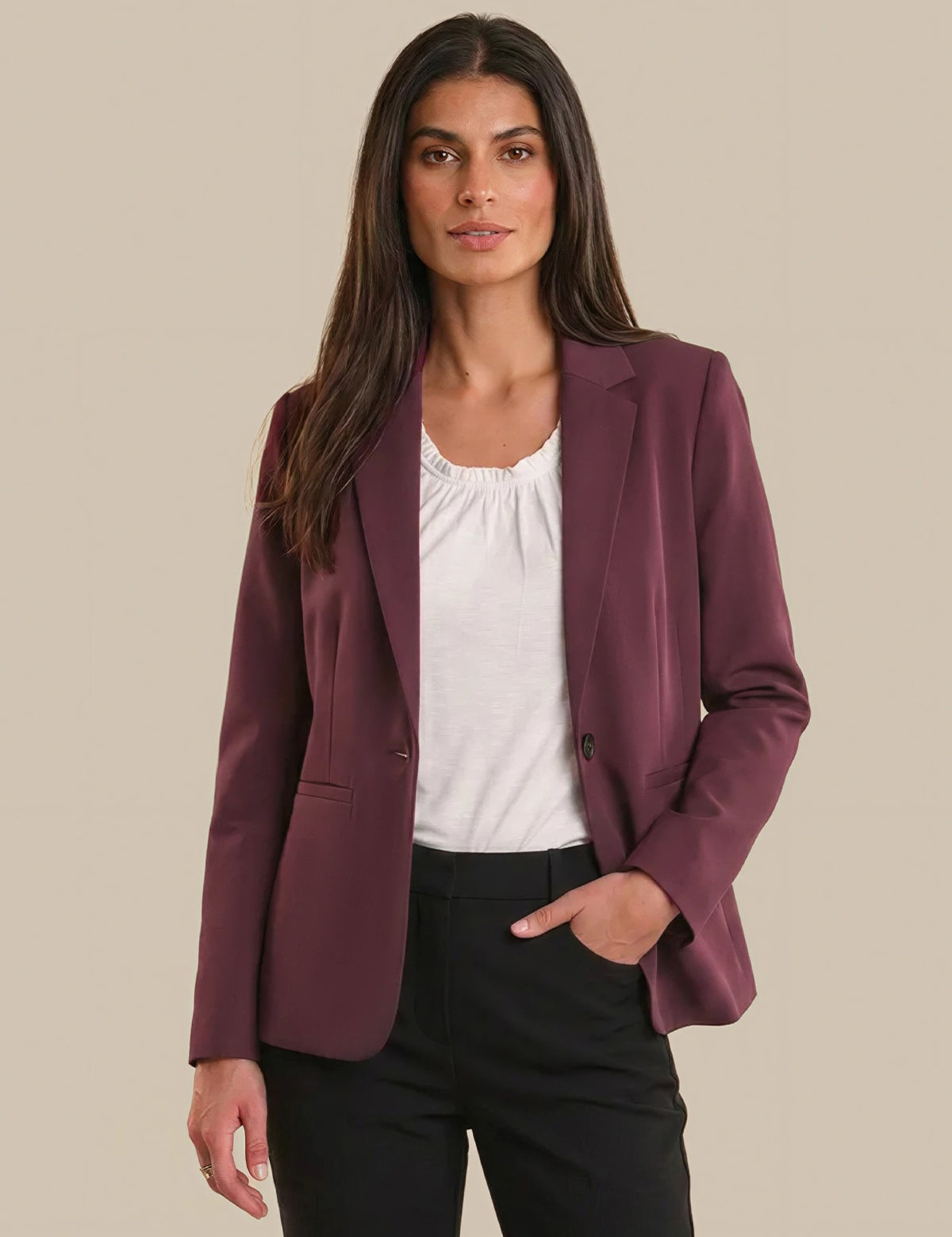 Woman wearing a burgundy blazer over a white top and black pants on a beige background