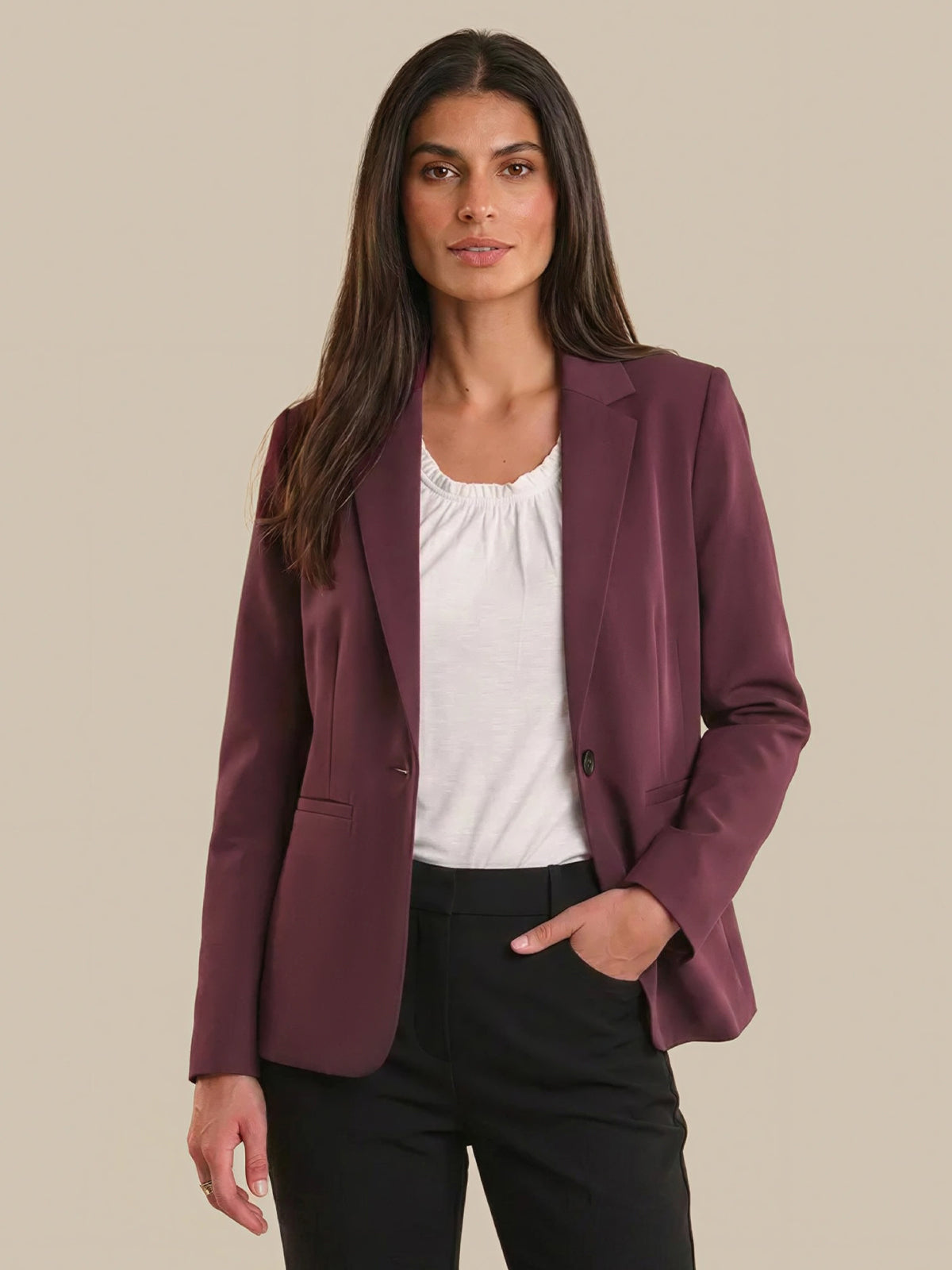 Woman wearing a burgundy blazer over a white top and black pants on a beige background