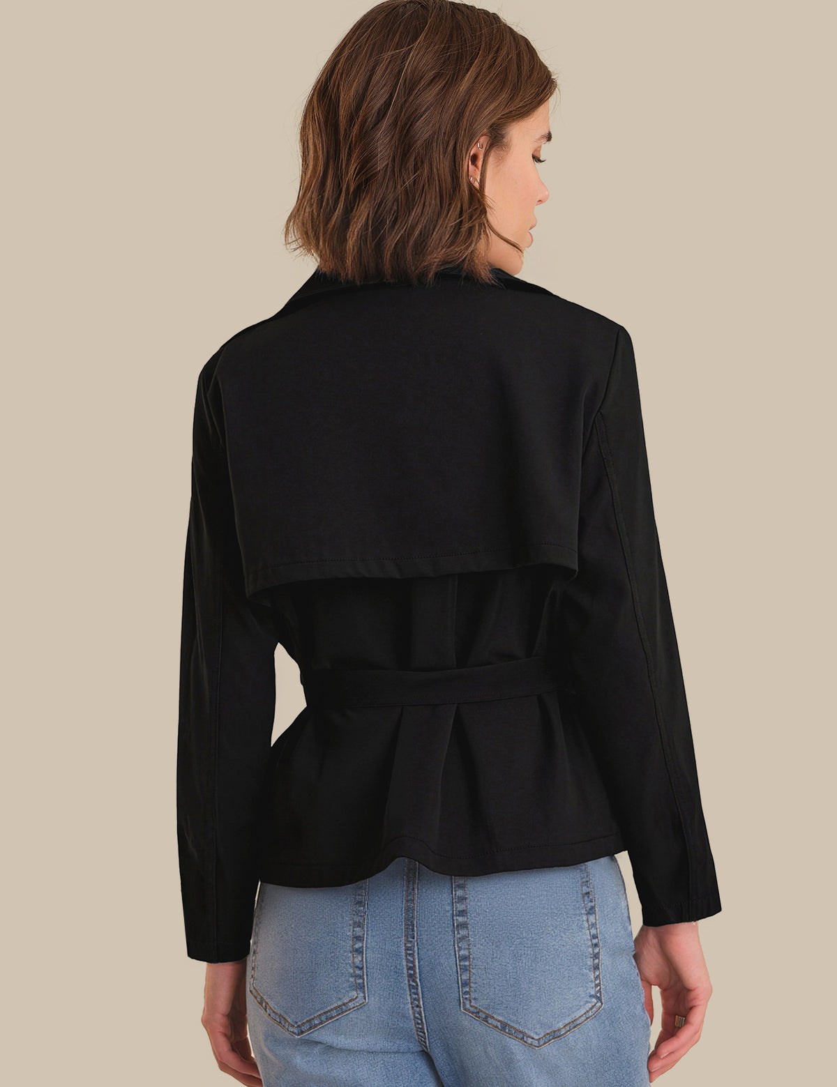 Person wearing a black jacket and light blue jeans on a beige background