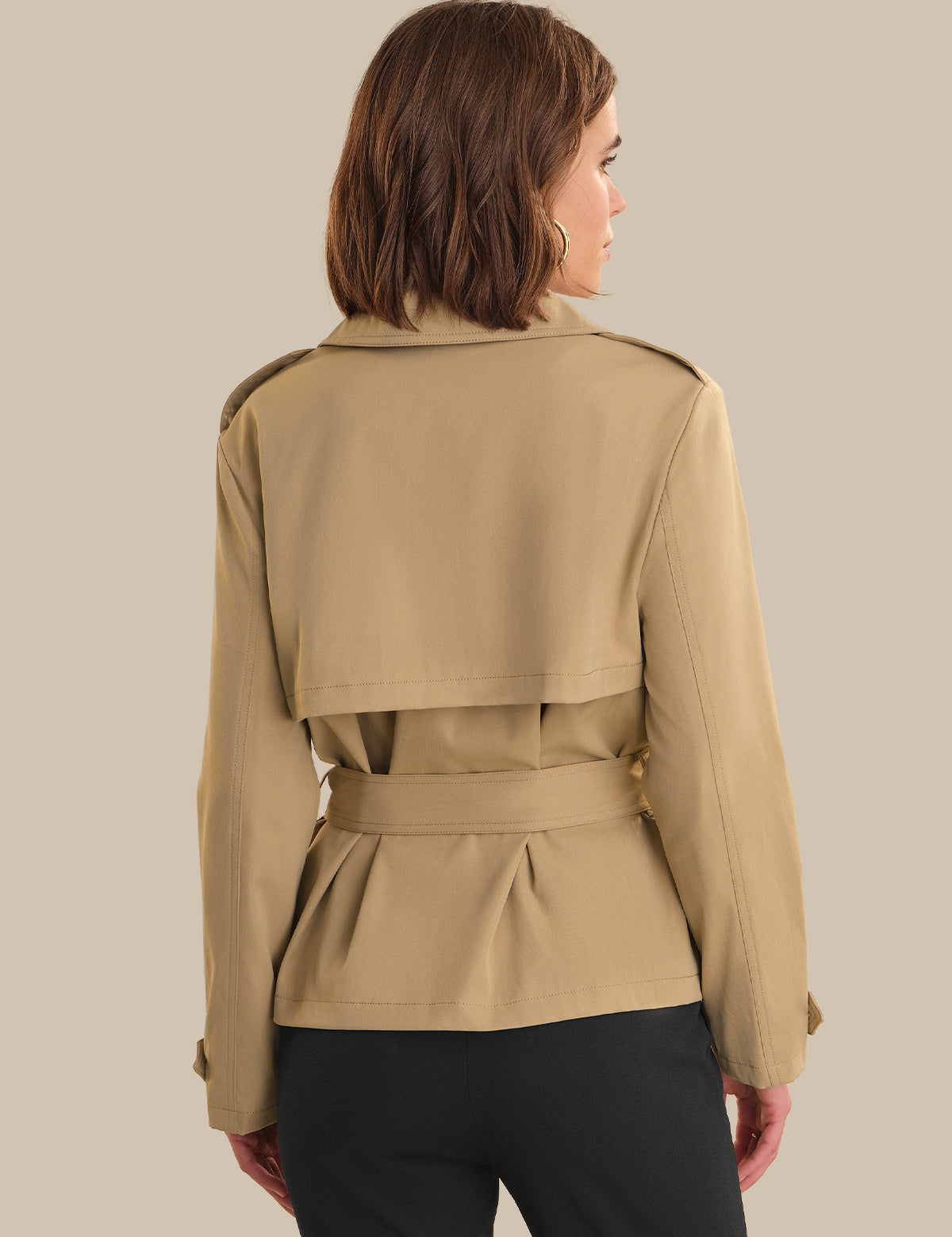 Woman wearing a beige trench coat against a plain background