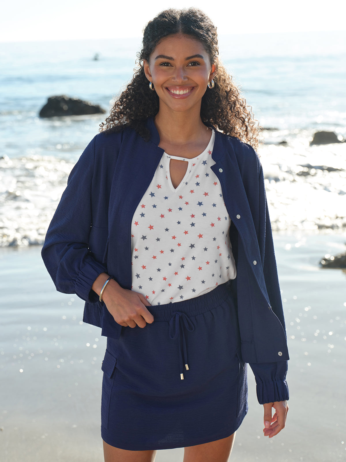Woman wearing a navy blue outfit with a white top with star pattern on a beach.