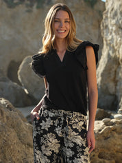 Woman wearing a black top and floral pants standing against a rocky background