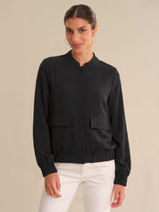 Woman wearing a black bomber jacket and white pants on a beige background