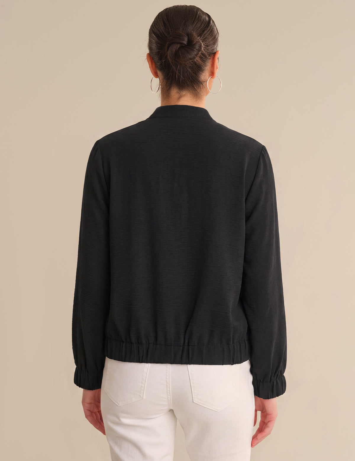 Person wearing a black jacket and white pants on a beige background