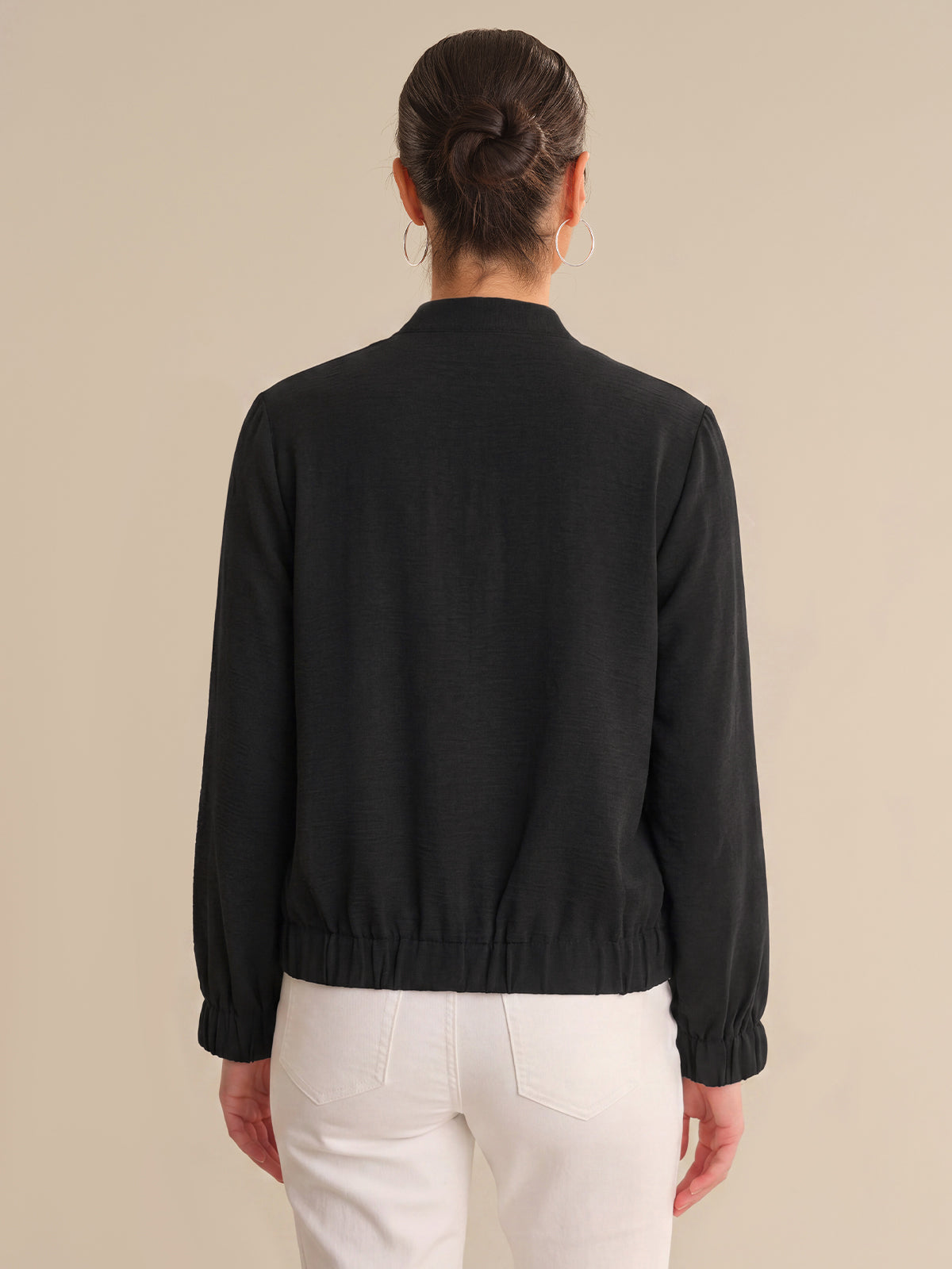 Person wearing a black jacket and white pants on a beige background